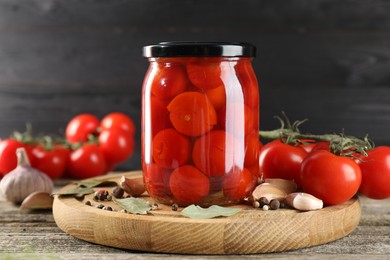 Tasty pickled tomatoes in jar, fresh vegetables and spices on wooden table