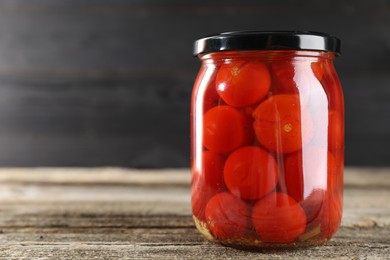 Tasty pickled tomatoes in jar on wooden table, closeup. Space for text