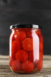 Photo of Tasty pickled tomatoes in jar on wooden table