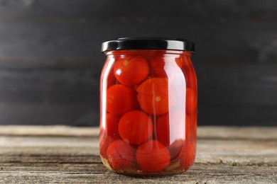 Photo of Tasty pickled tomatoes in jar on wooden table