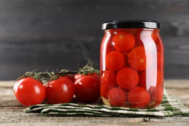 Tasty pickled tomatoes in jar and fresh vegetables on wooden table