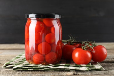 Tasty pickled tomatoes in jar and fresh vegetables on wooden table