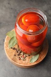 Photo of Tasty pickled tomatoes in jar, bay leaves and peppercorns on grey table
