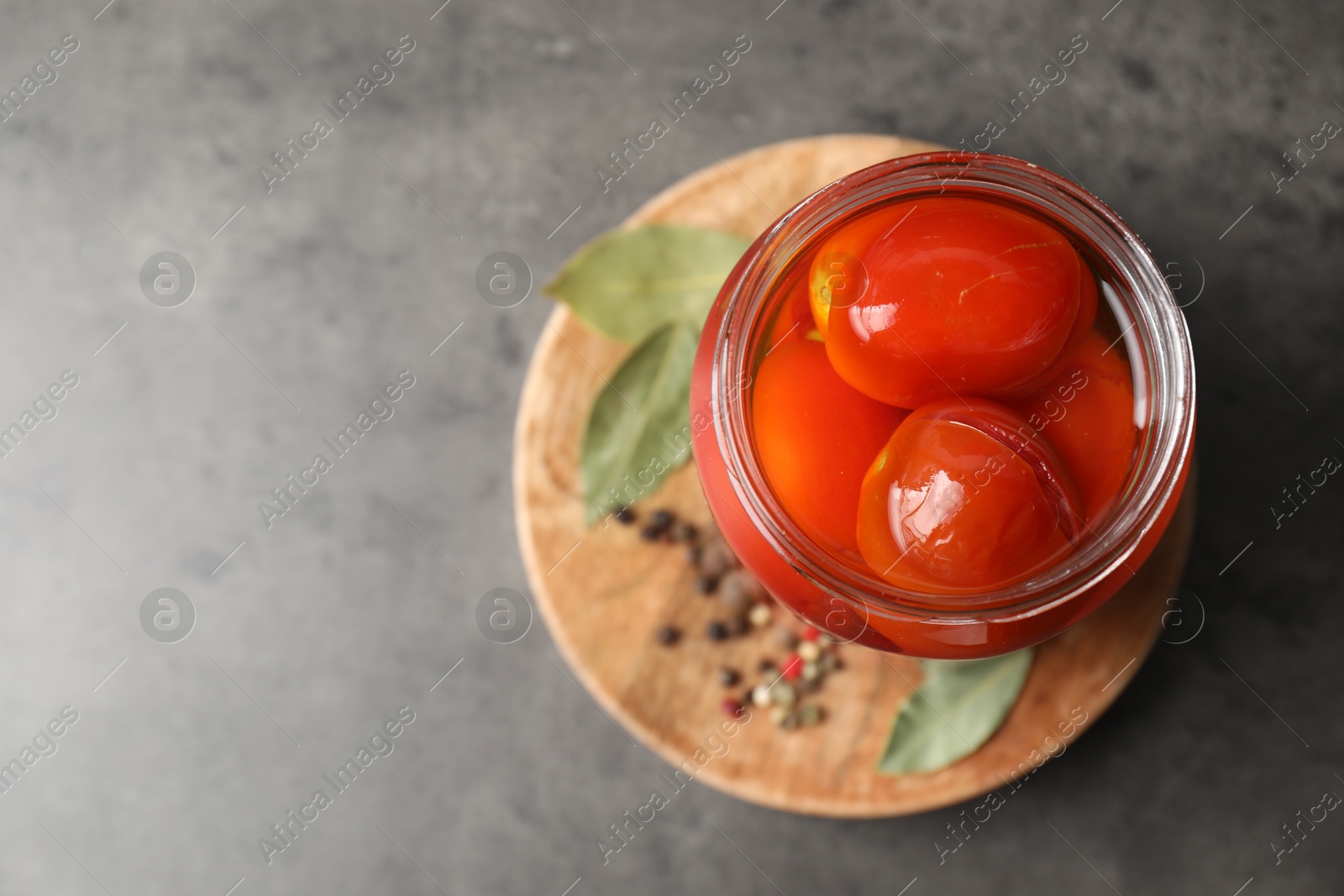 Photo of Tasty pickled tomatoes in jar, bay leaves and peppercorns on grey table, top view. Space for text