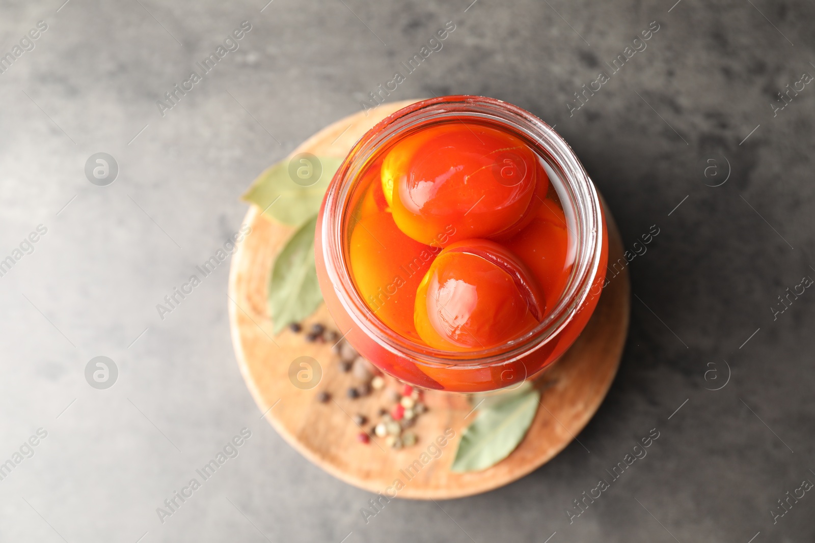 Photo of Tasty pickled tomatoes in jar, bay leaves and peppercorns on grey table, top view