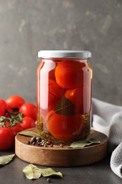 Tasty pickled tomatoes in jar, spices and fresh vegetables on grey table