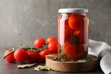 Photo of Tasty pickled tomatoes in jar, spices and fresh vegetables on grey table. Space for text