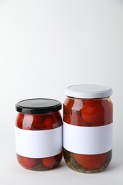 Tasty pickled tomatoes in jars on light background. Space for text