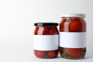 Photo of Tasty pickled tomatoes in jars on light background, closeup. Space for text