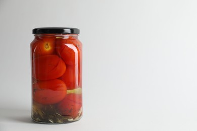 Tasty pickled tomatoes in jar on light grey background. Space for text