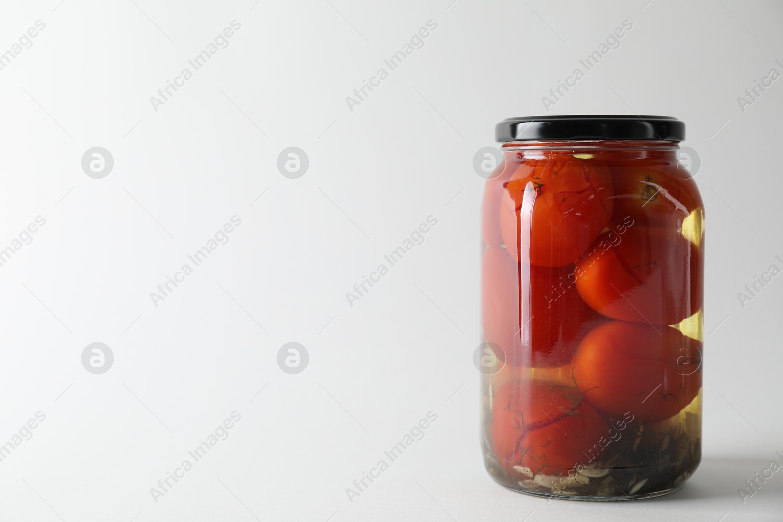 Photo of Tasty pickled tomatoes in jar on light grey background. Space for text