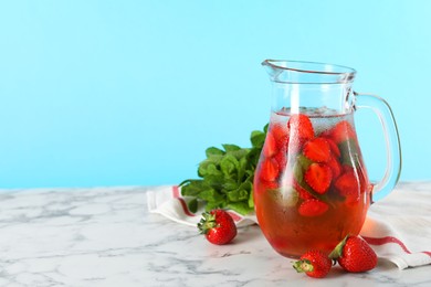 Photo of Tasty strawberry lemonade with mint in jug and berries on white marble table against light blue background. Space for text