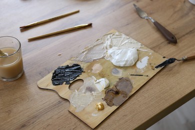 Photo of Palette with paints and tools on wooden table, closeup