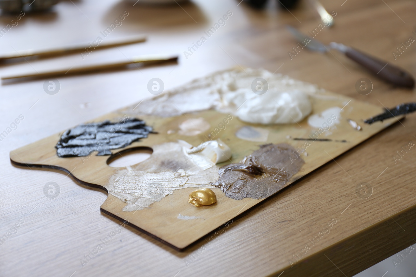 Photo of Palette with paints on wooden table, closeup
