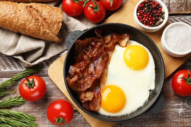 Photo of Tasty bacon and eggs in dish among products on wooden table, flat lay