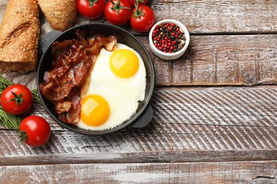 Tasty bacon and eggs in dish among products on wooden table, flat lay. Space for text