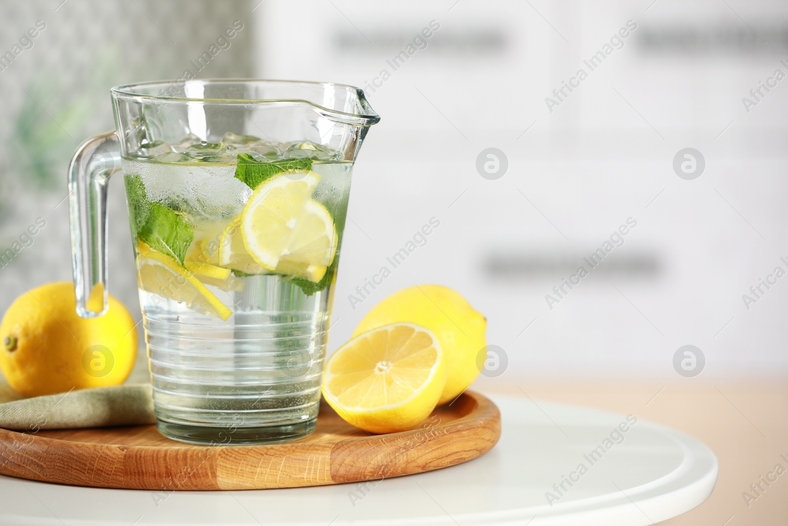 Photo of Refreshing lemonade with mint in jug and citrus fruits on white table. Space for text