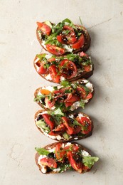 Delicious bruschettas with ricotta cheese, tomatoes and arugula on light textured table, flat lay