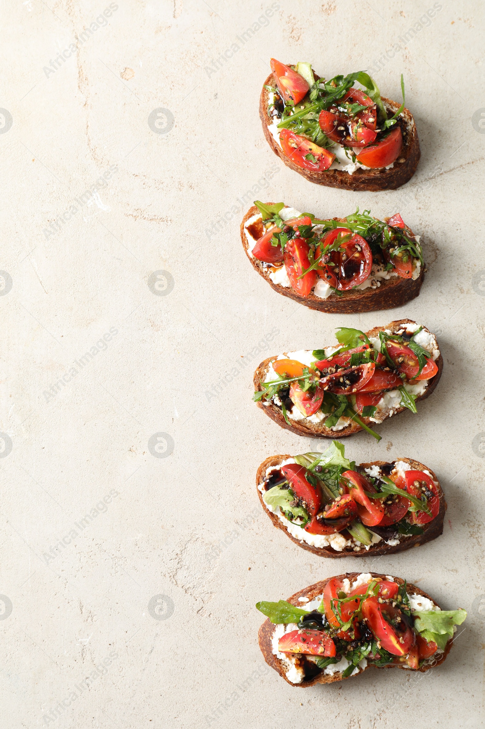 Photo of Delicious bruschettas with ricotta cheese, tomatoes and arugula on light textured table, flat lay. Space for text