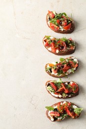Delicious bruschettas with ricotta cheese, tomatoes and arugula on light textured table, flat lay. Space for text