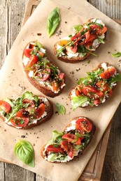Photo of Delicious ricotta bruschettas with tomatoes, arugula and basil on wooden table, top view