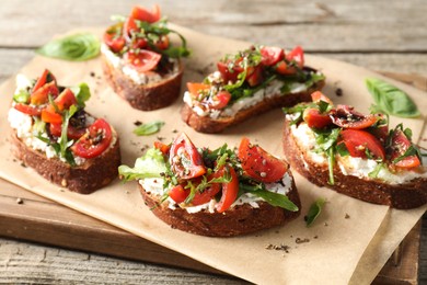 Photo of Delicious ricotta bruschettas with tomatoes and arugula on wooden table, closeup