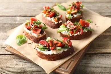 Delicious ricotta bruschettas with tomatoes and arugula on wooden table, closeup