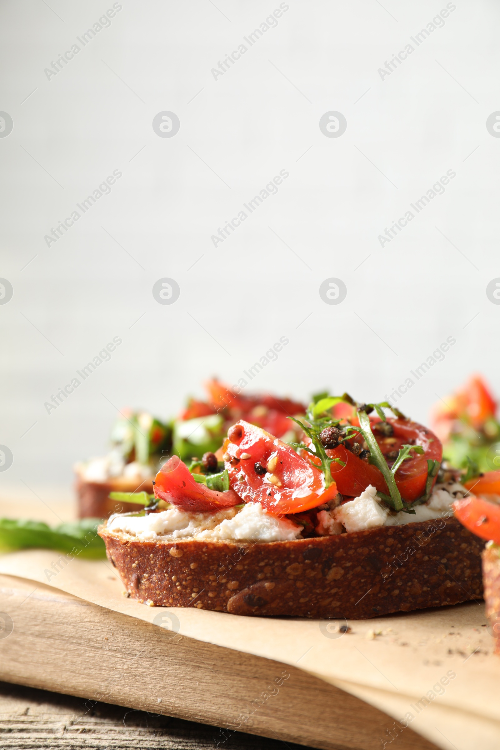 Photo of Delicious ricotta bruschettas with tomatoes and arugula on wooden table, closeup. Space for text