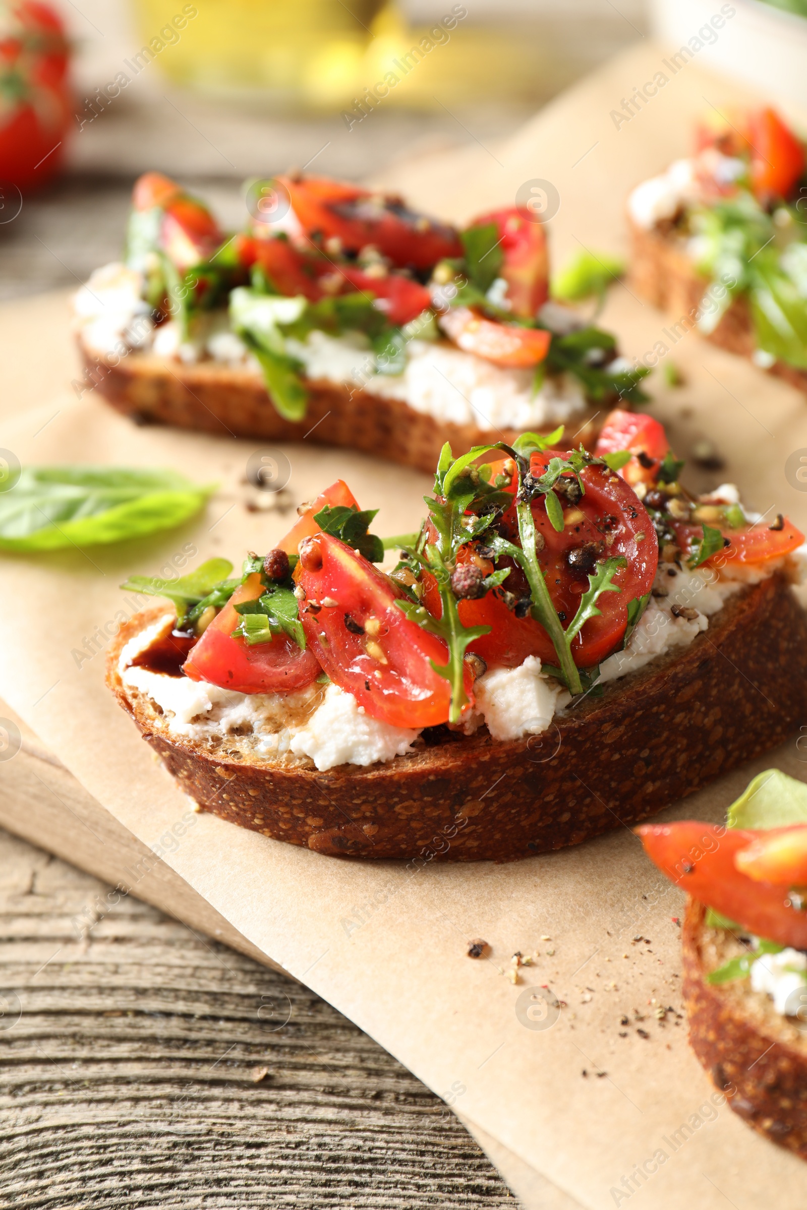 Photo of Delicious ricotta bruschettas with tomatoes, arugula and basil on wooden table, closeup