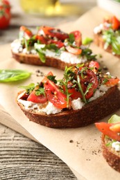 Photo of Delicious ricotta bruschettas with tomatoes, arugula and basil on wooden table, closeup