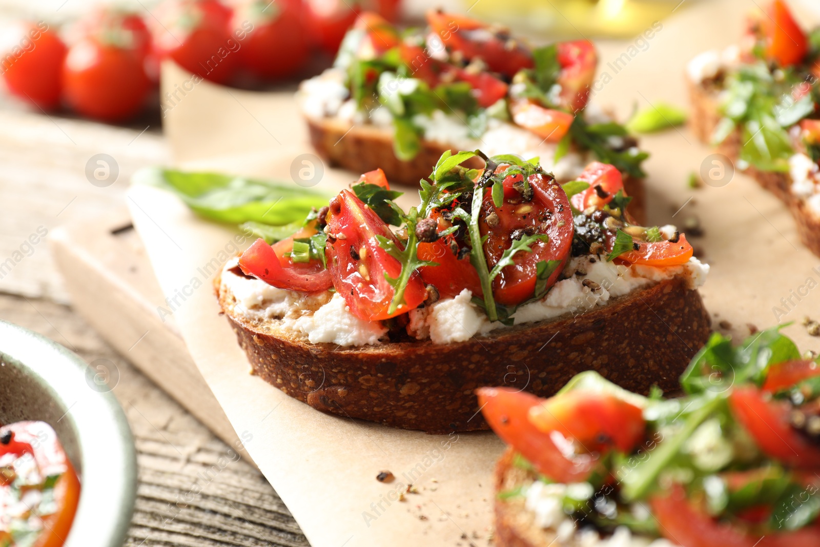 Photo of Delicious ricotta bruschettas with tomatoes, arugula and basil on wooden table, closeup