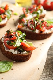 Photo of Delicious ricotta bruschettas with tomatoes, arugula and basil on wooden table, closeup