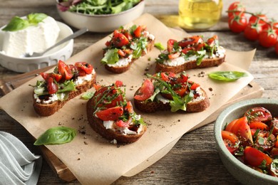 Delicious ricotta bruschettas with tomatoes, arugula and basil on wooden table, closeup