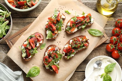 Delicious ricotta bruschettas with tomatoes, arugula and basil on wooden table, flat lay