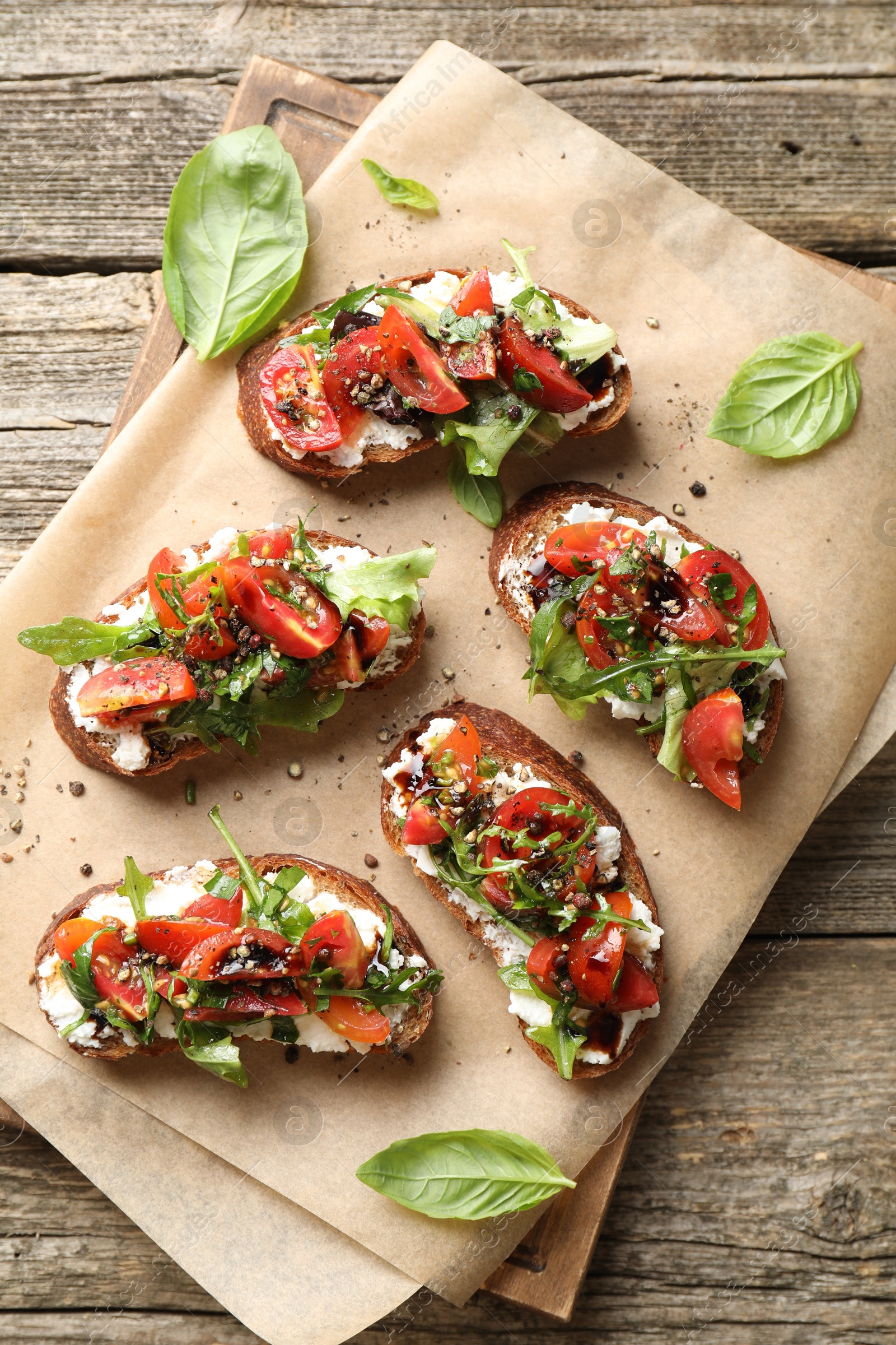 Photo of Delicious ricotta bruschettas with tomatoes, arugula and basil on wooden table, top view