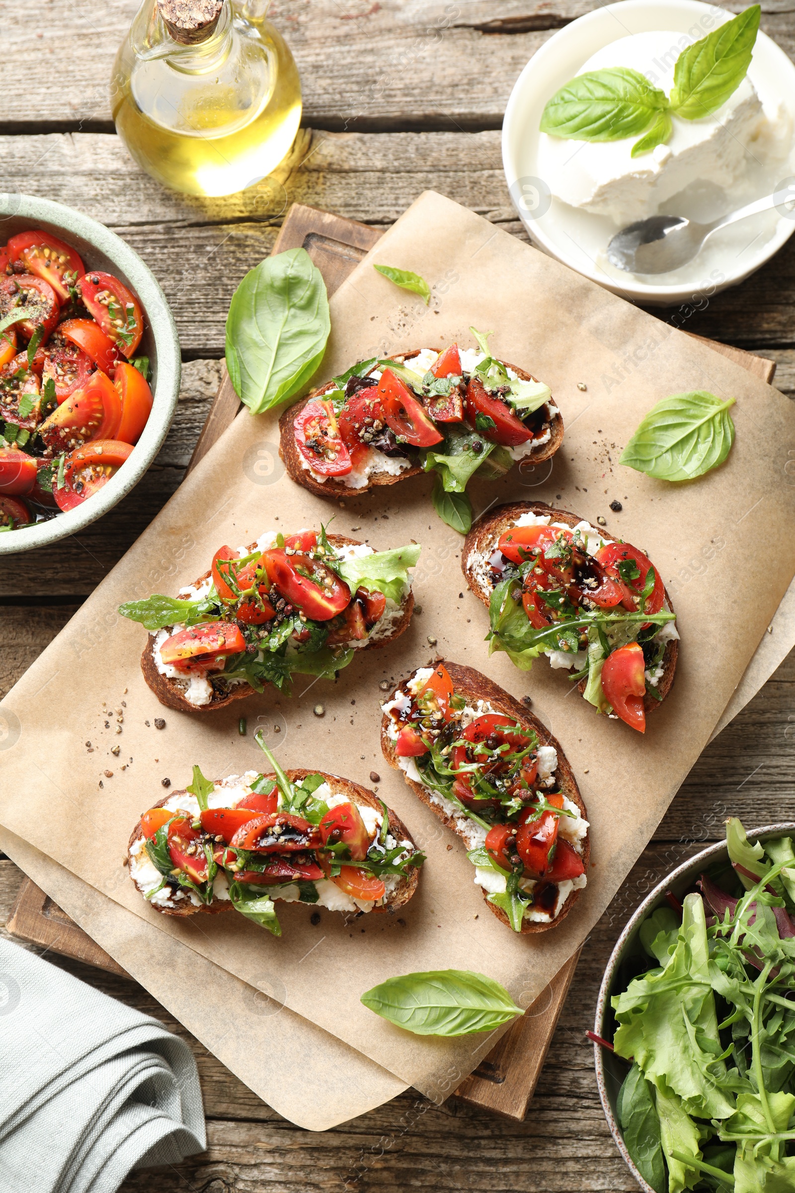 Photo of Delicious ricotta bruschettas with tomatoes, arugula and basil on wooden table, flat lay