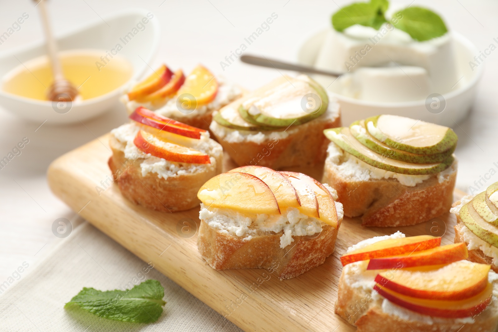 Photo of Delicious ricotta bruschettas with pears and apricots on white table, closeup