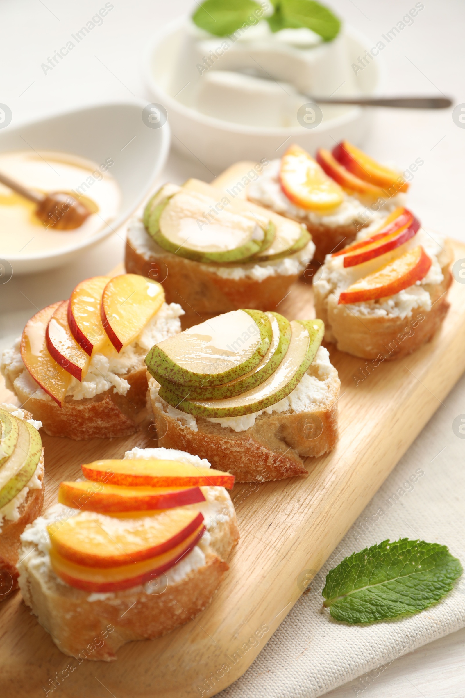 Photo of Delicious ricotta bruschettas with pears and apricots on white table, closeup