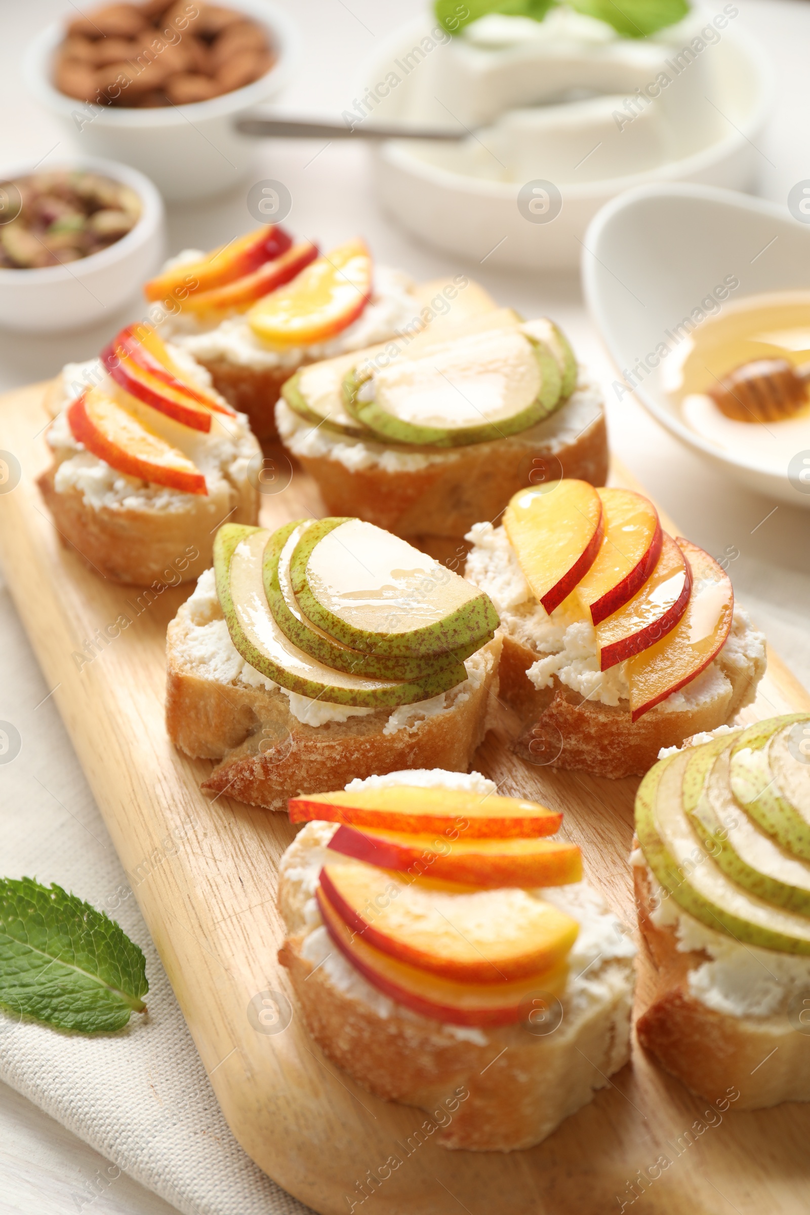 Photo of Delicious ricotta bruschettas with pears and apricots on white table, closeup