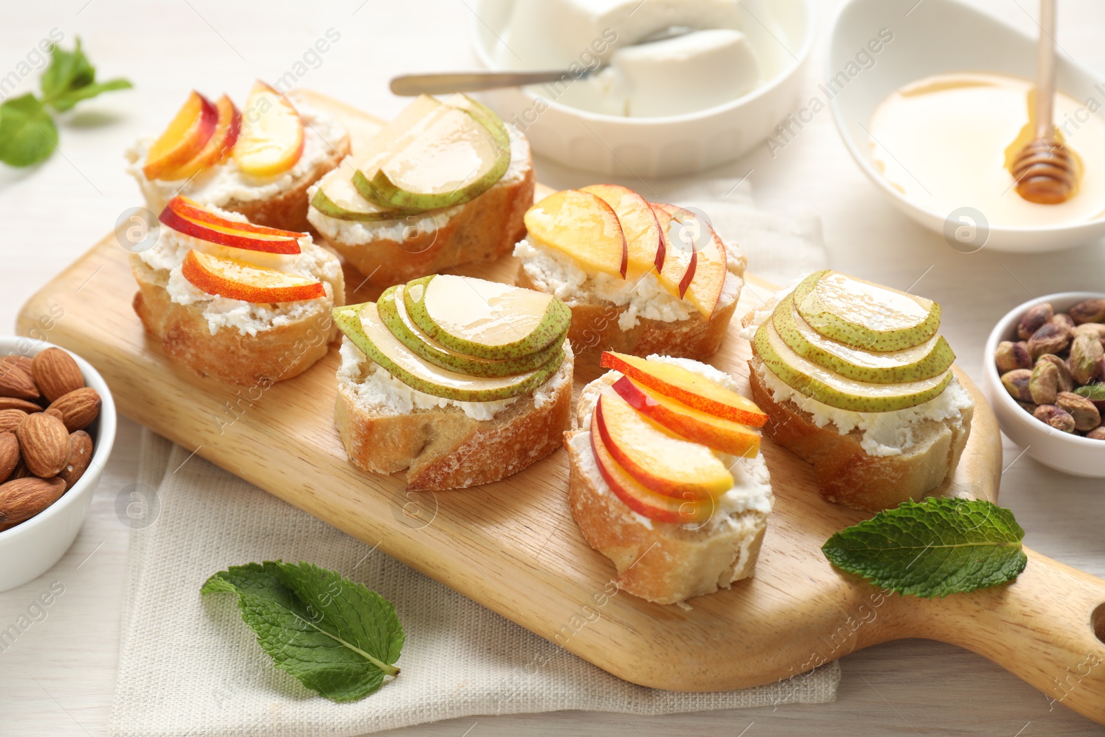 Photo of Delicious ricotta bruschettas with pears, apricots, nuts and mint on white wooden table, closeup