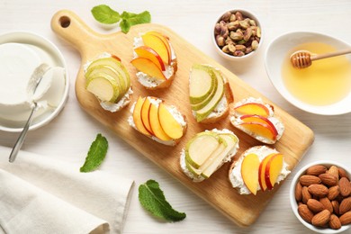 Photo of Delicious ricotta bruschettas with pears and apricots among products on white wooden table, flat lay