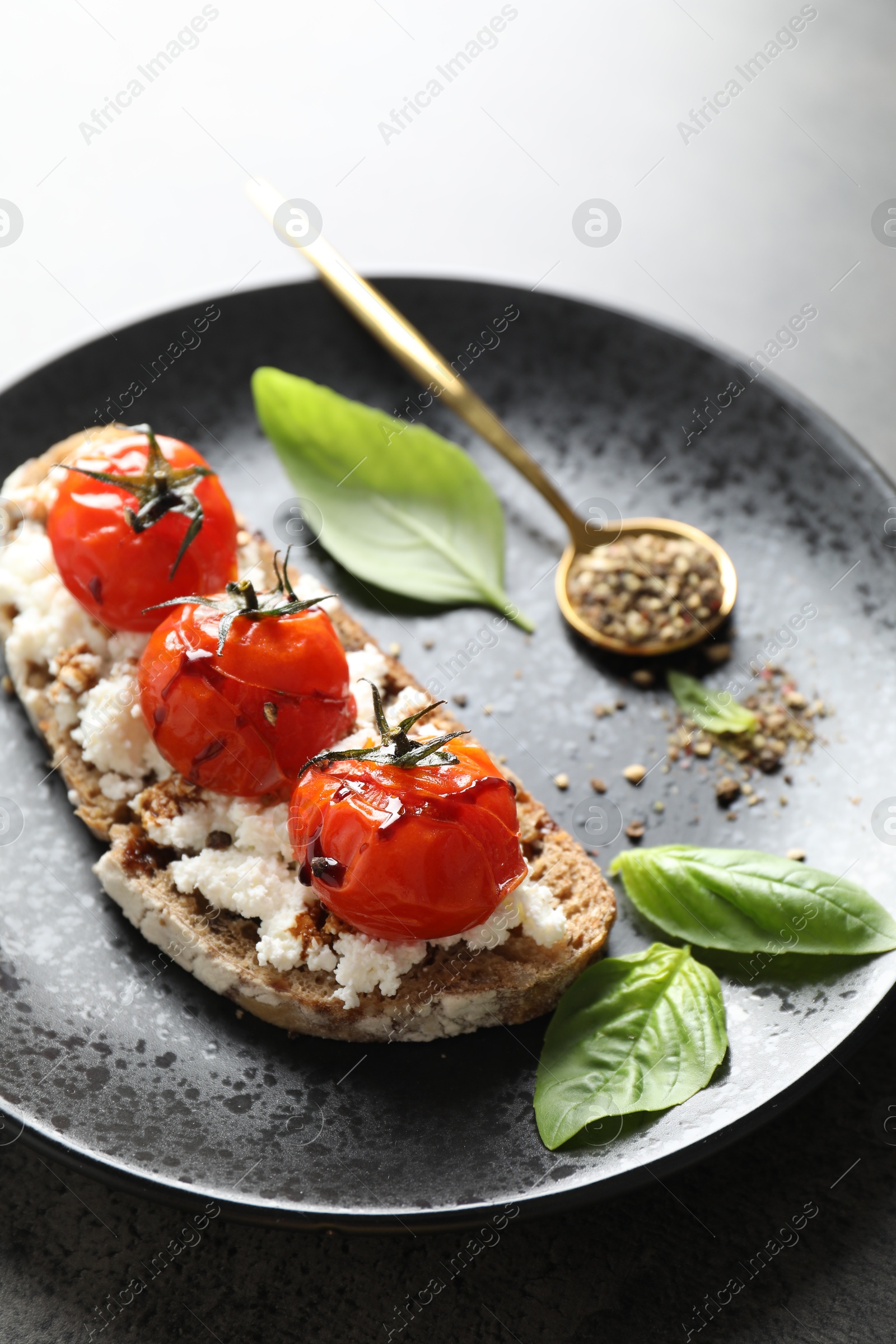 Photo of Delicious ricotta bruschetta with sun dried tomatoes, sauce, basil and milled pepper on grey table, closeup