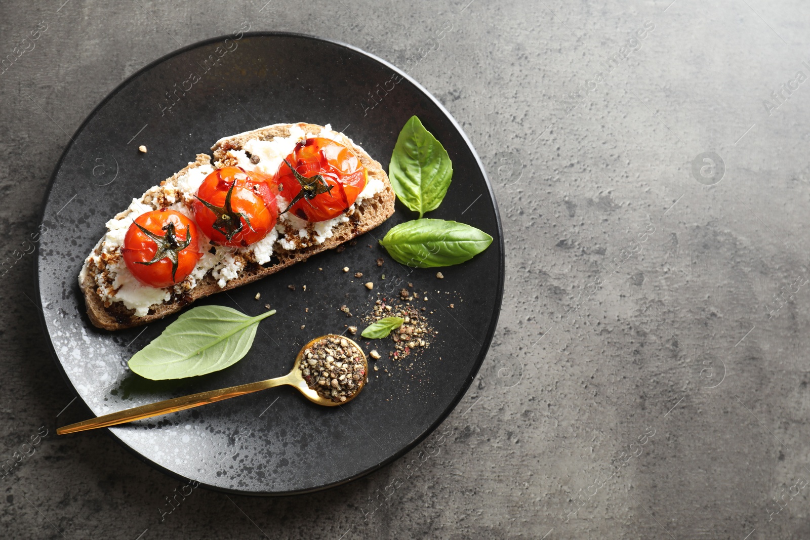 Photo of Delicious ricotta bruschetta with sun dried tomatoes, sauce, basil and milled pepper on grey textured table, top view. Space for text