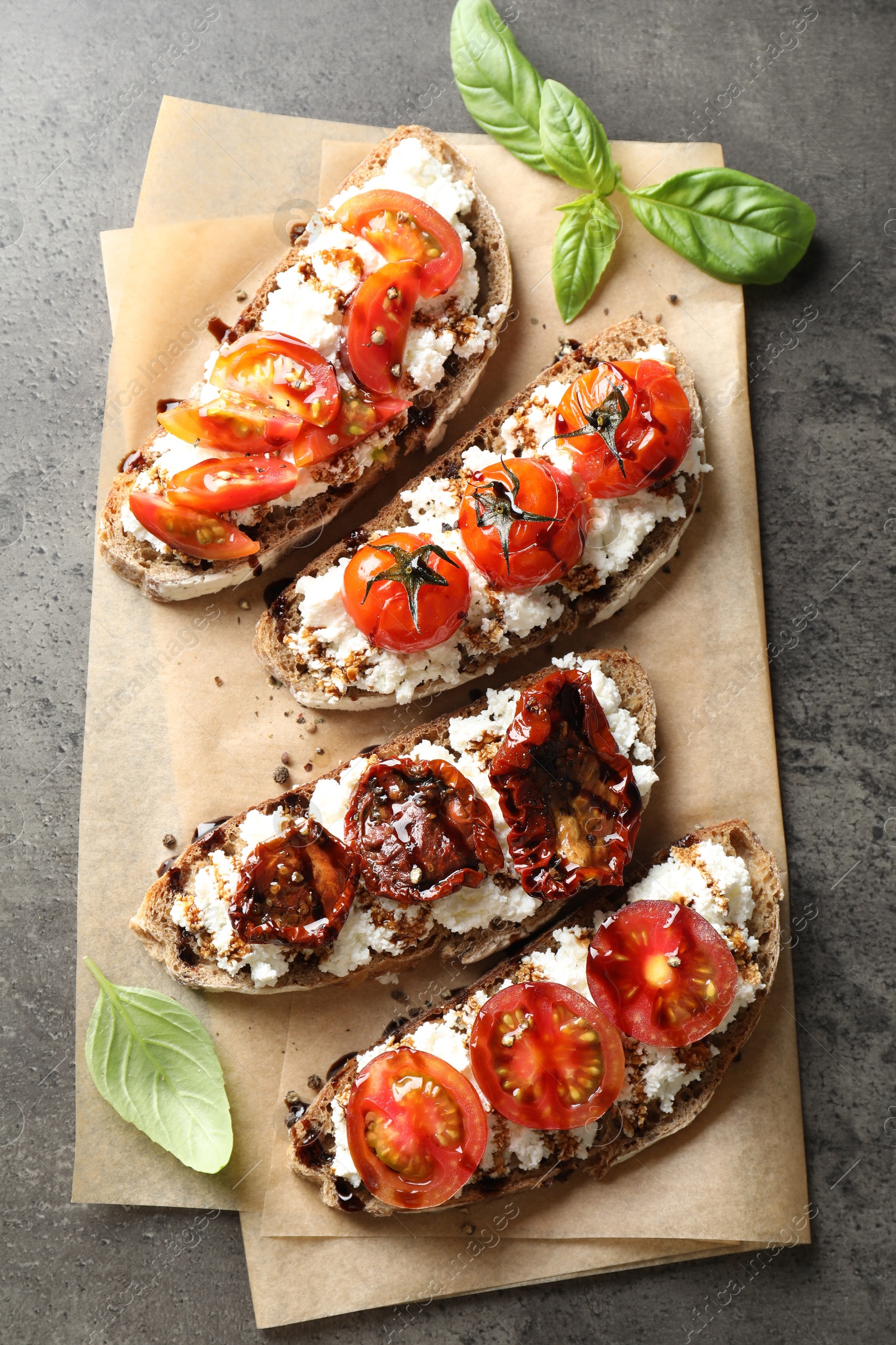 Photo of Delicious ricotta bruschettas with sun dried tomatoes, sauce and basil on grey textured table, top view