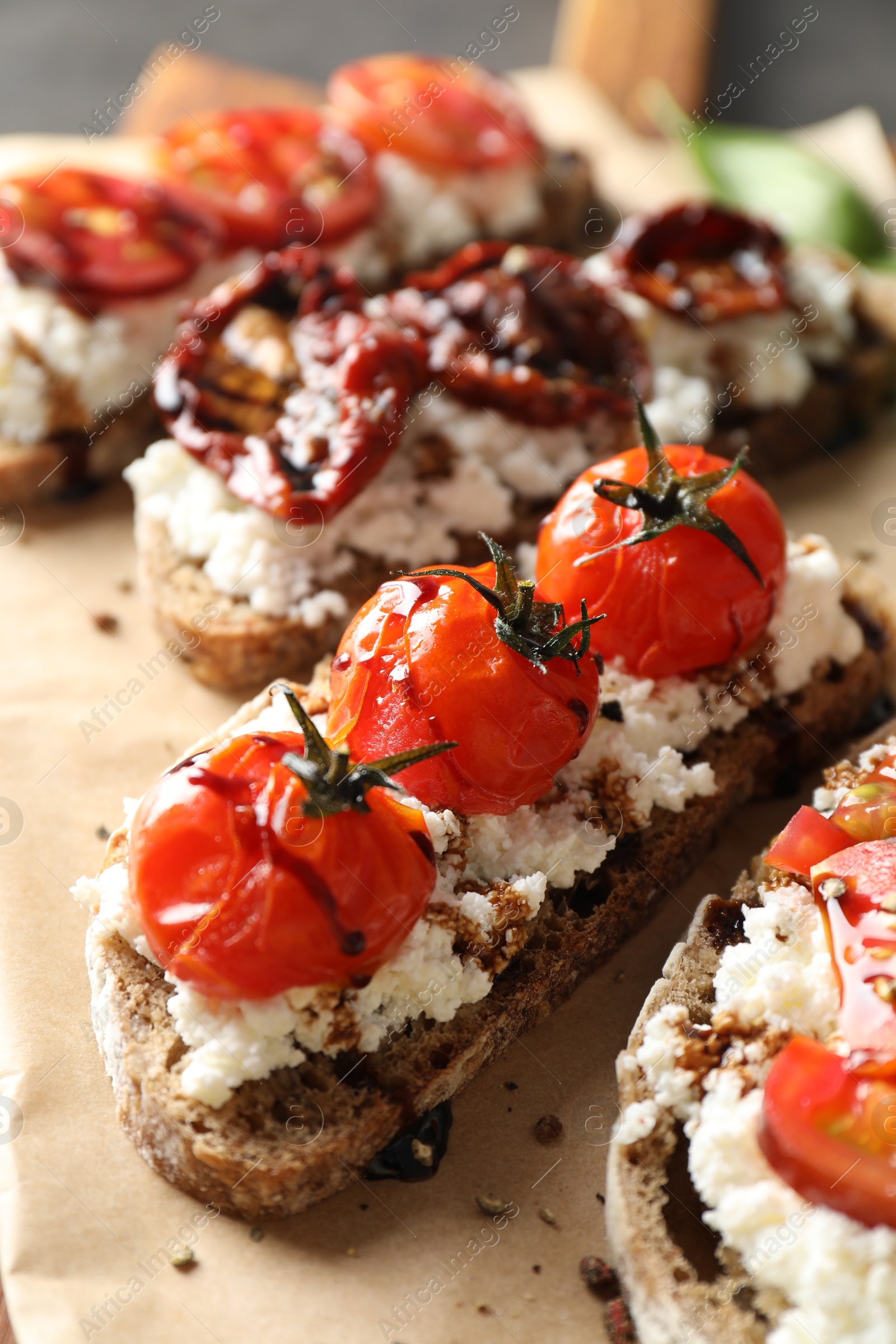 Photo of Delicious ricotta bruschettas with sun dried tomatoes and sauce on parchment, closeup