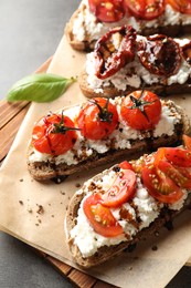 Photo of Delicious ricotta bruschettas with sun dried tomatoes, sauce and basil on grey textured table, above view