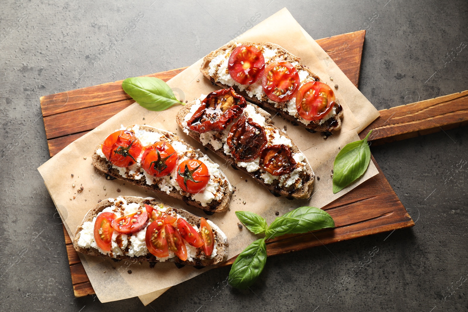 Photo of Delicious ricotta bruschettas with sun dried tomatoes, sauce and basil on grey textured table, top view