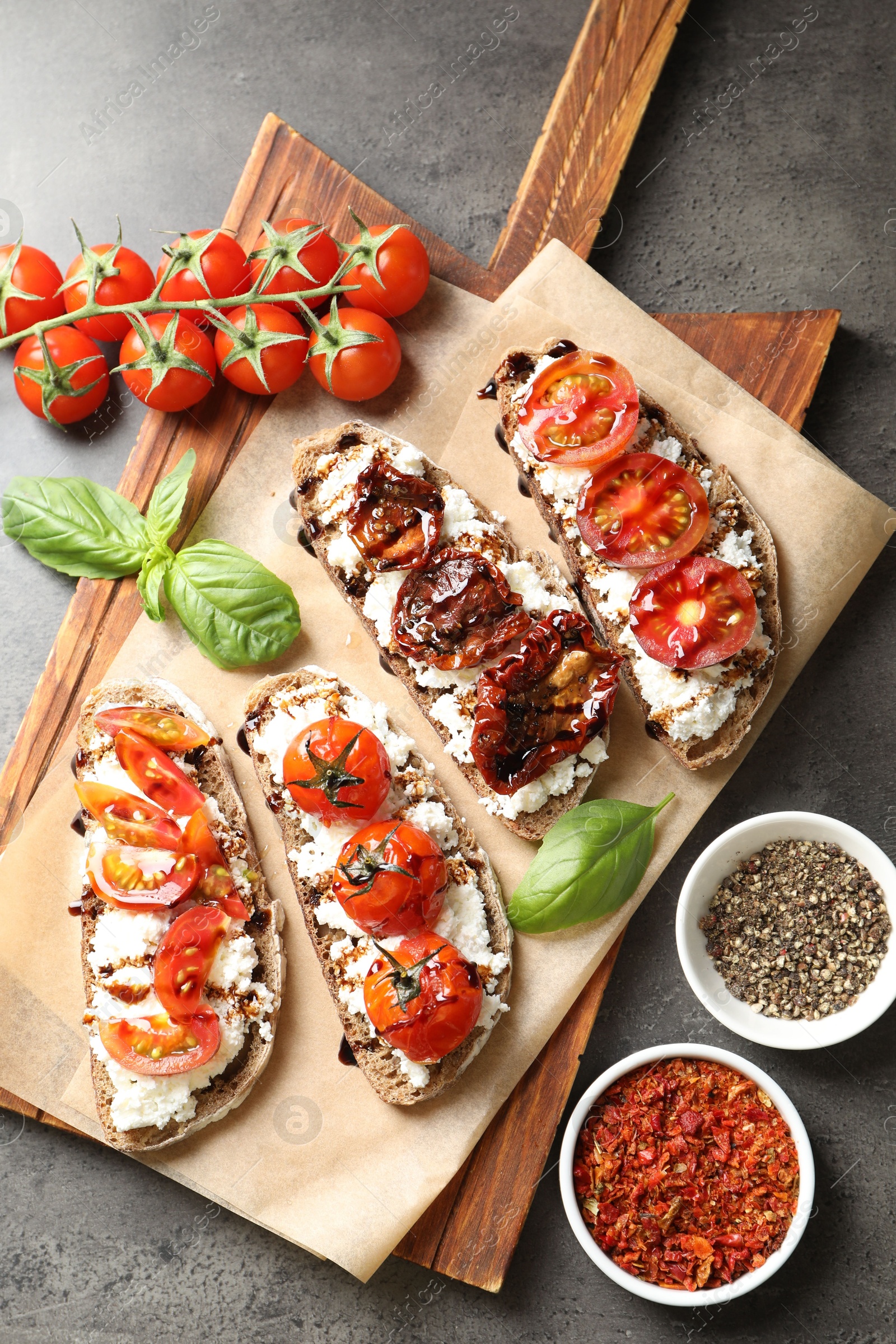 Photo of Delicious ricotta bruschettas with sun dried tomatoes, spices and basil on grey textured table, flat lay