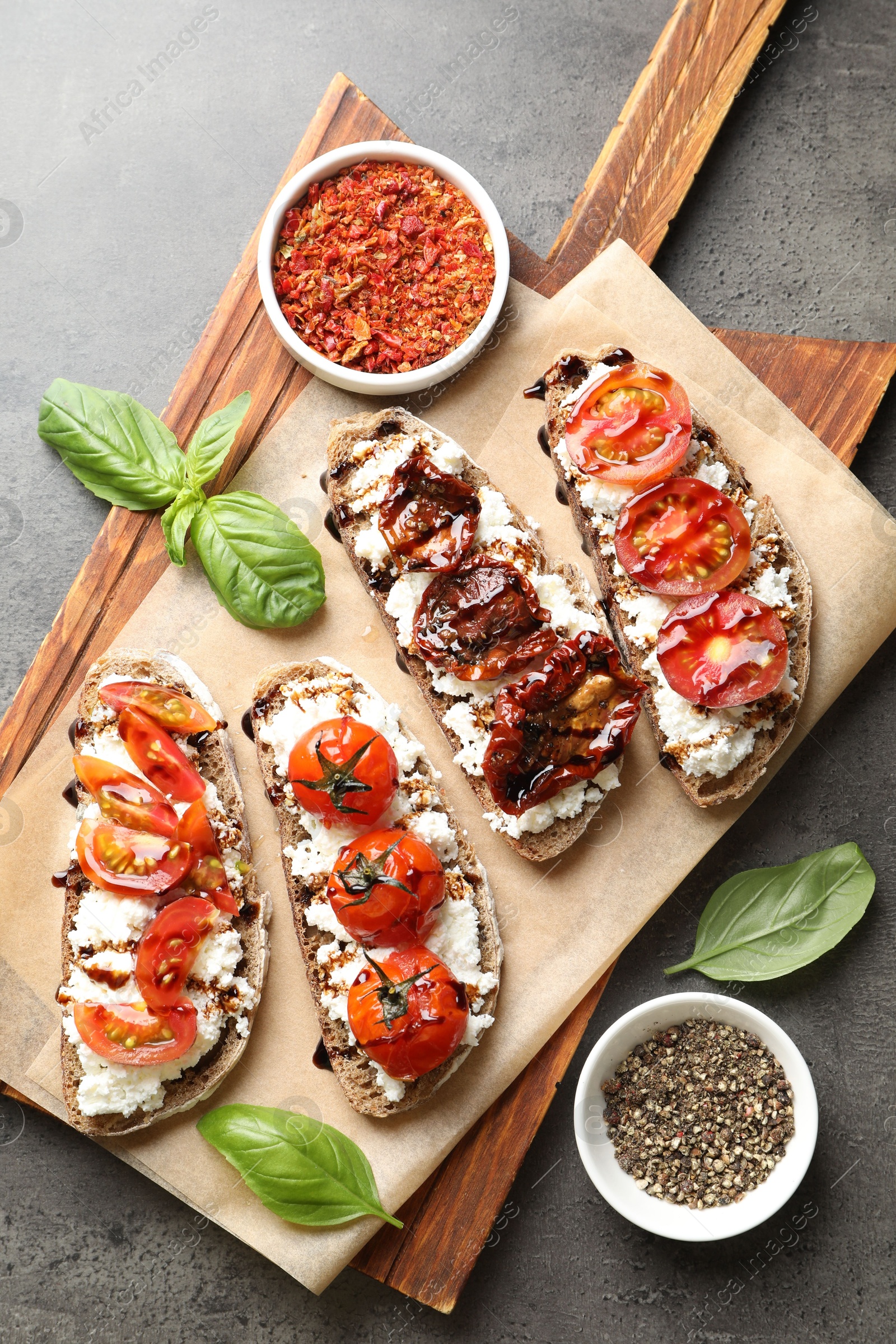 Photo of Delicious ricotta bruschettas with sun dried tomatoes, spices and basil on grey textured table, flat lay