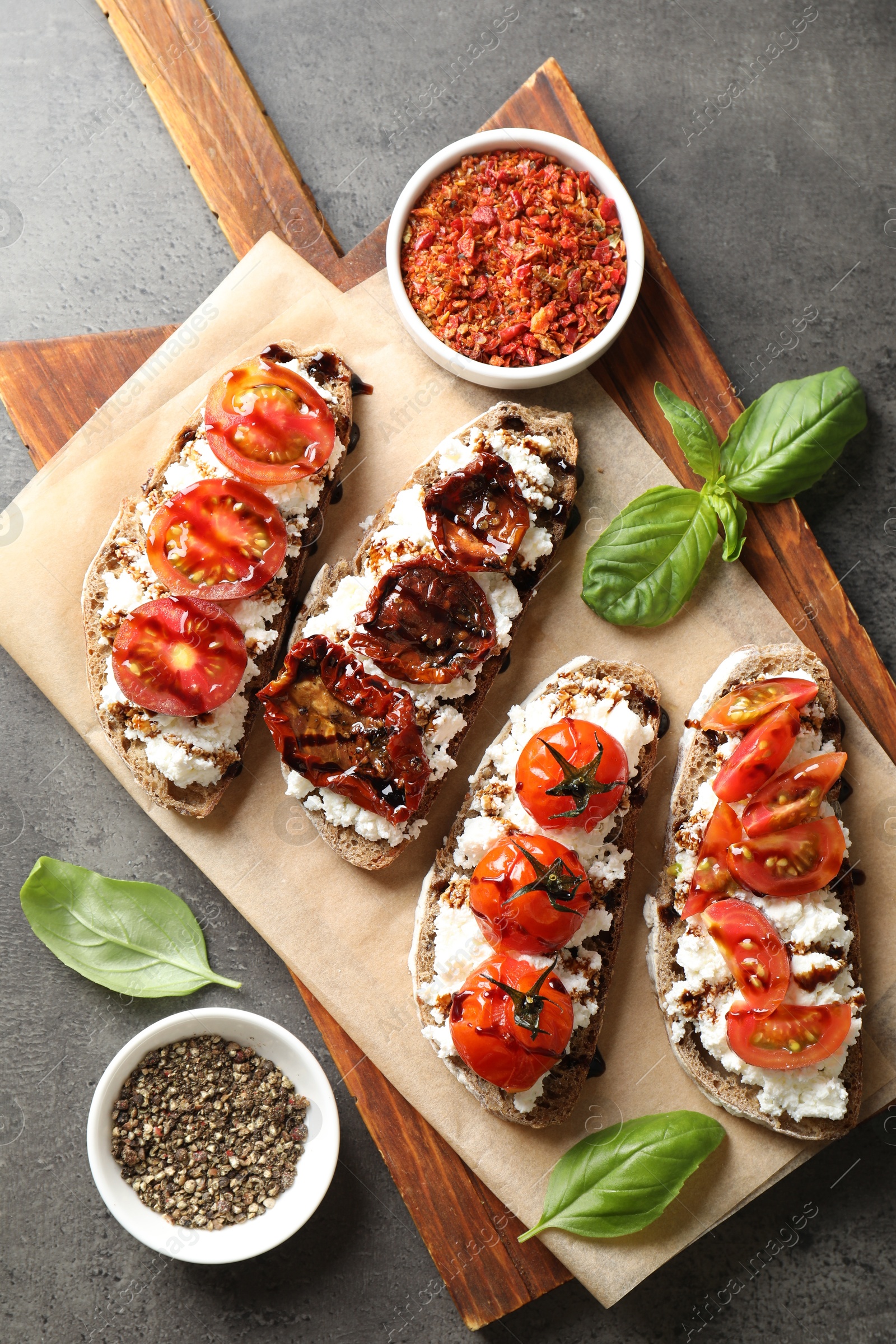 Photo of Delicious ricotta bruschettas with sun dried tomatoes, spices and basil on grey textured table, flat lay